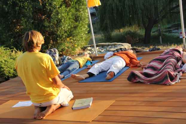 Yoga class with teacher sitting observing 3 students lying in savasana