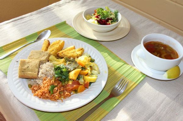 Meal place setting of bowl of soup, bowl of salad, and plate of potatoes, roast vegetables, grains, herbs and bread.