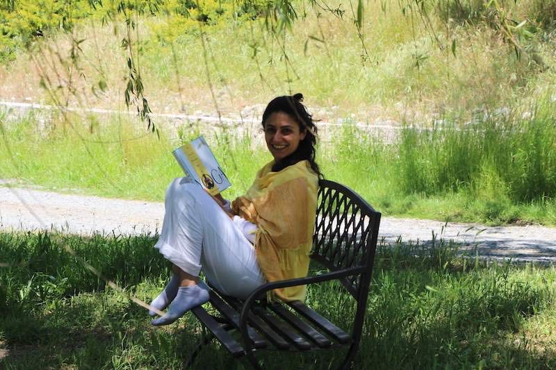 Woman sitting on a bench reading the "Complete Illustrated Book of Yoga"